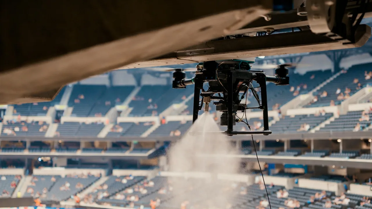 Close-up of AeroWash drone spraying cleaning solution inside a sports stadium with seating visible